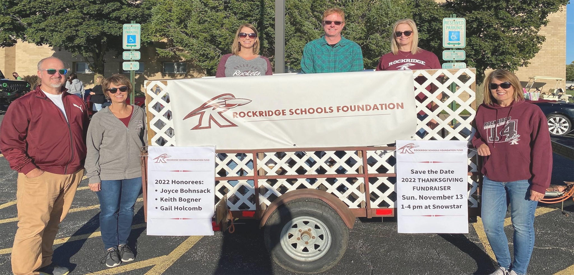 Representatives of the Rockridge Schools Foundation stand in a parade float. Several other representatives stand to each side of the float. The parade float has signs recognizing 2022 honorees and advertising an event