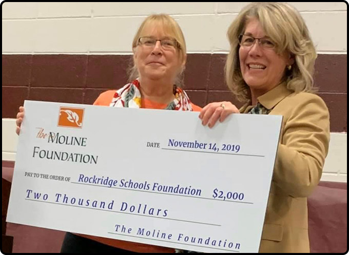 One woman presents a check donating to the Rockridge Schools Foundation to another woman